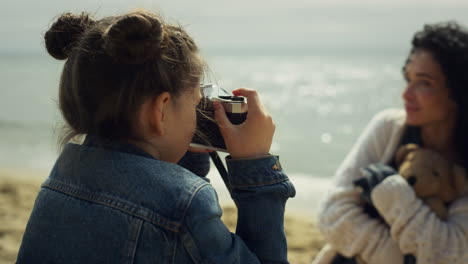 small girl taking photo on family sea vacation. mother daughter bonding outside.