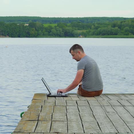 handsome man sits on a wooden pier with laptop. work on vacation