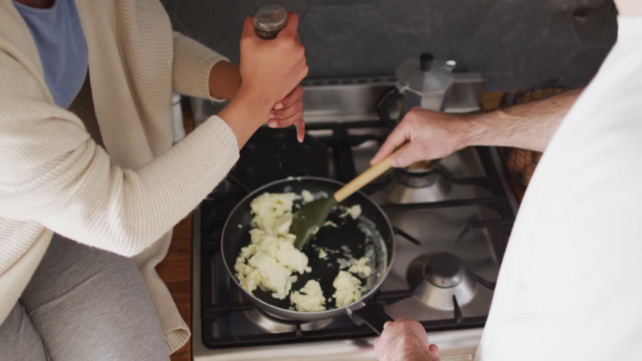 video de ángulo alto de una pareja feliz y diversa riendo y cocinando huevos revueltos en la cocina