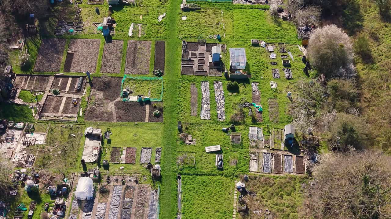 İngiltere'nin Hertford Heath bölgesindeki hobi bahçeleri üzerinde ilkbaharda geri geri giden bir drone, berrak bir günde yukarıdan bahçe parsellerini, kulübeleri, yeşil yolları ve kırsal manzarayı ortaya çıkarıyor.
