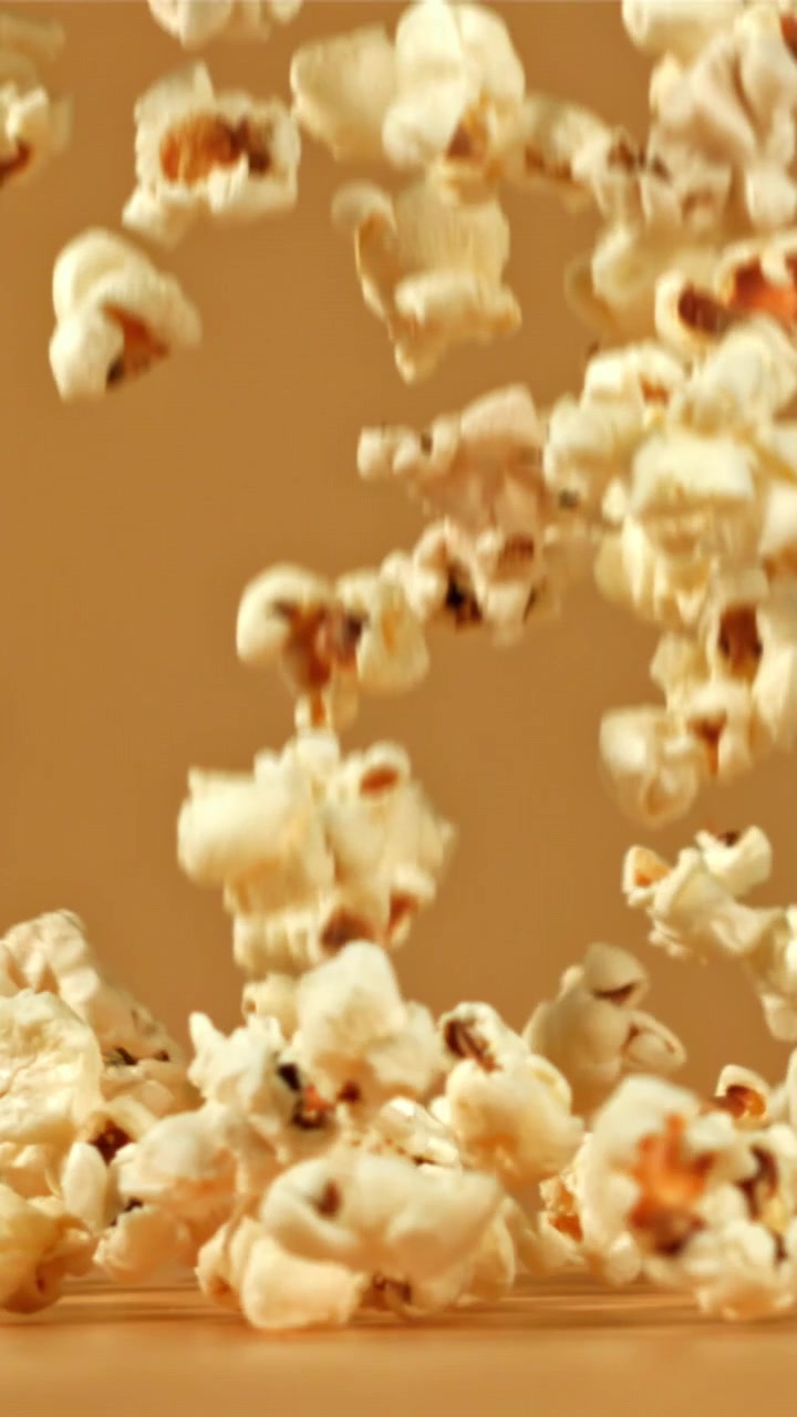 Popcorn che cadono e si accumulano su uno sfondo marrone al rallentatore.