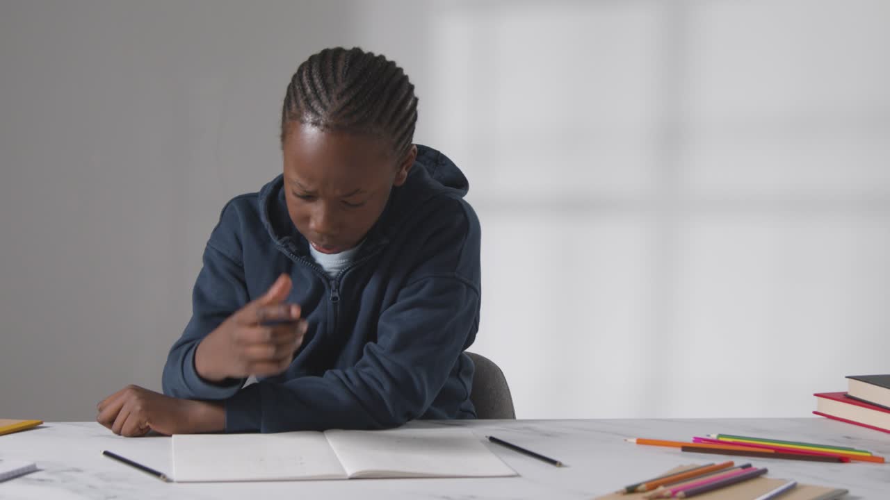 Studio Shot Of Boy At Table Struggling To Concentrate On School Book 