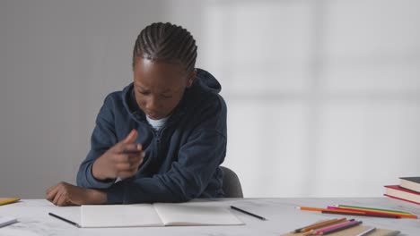 studio shot of boy at table struggling to concentrate on school book