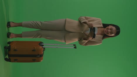 full body of asian businesswoman traveler with luggage looking at the passport and looking around while standing in the green screen background studio, during sunset time