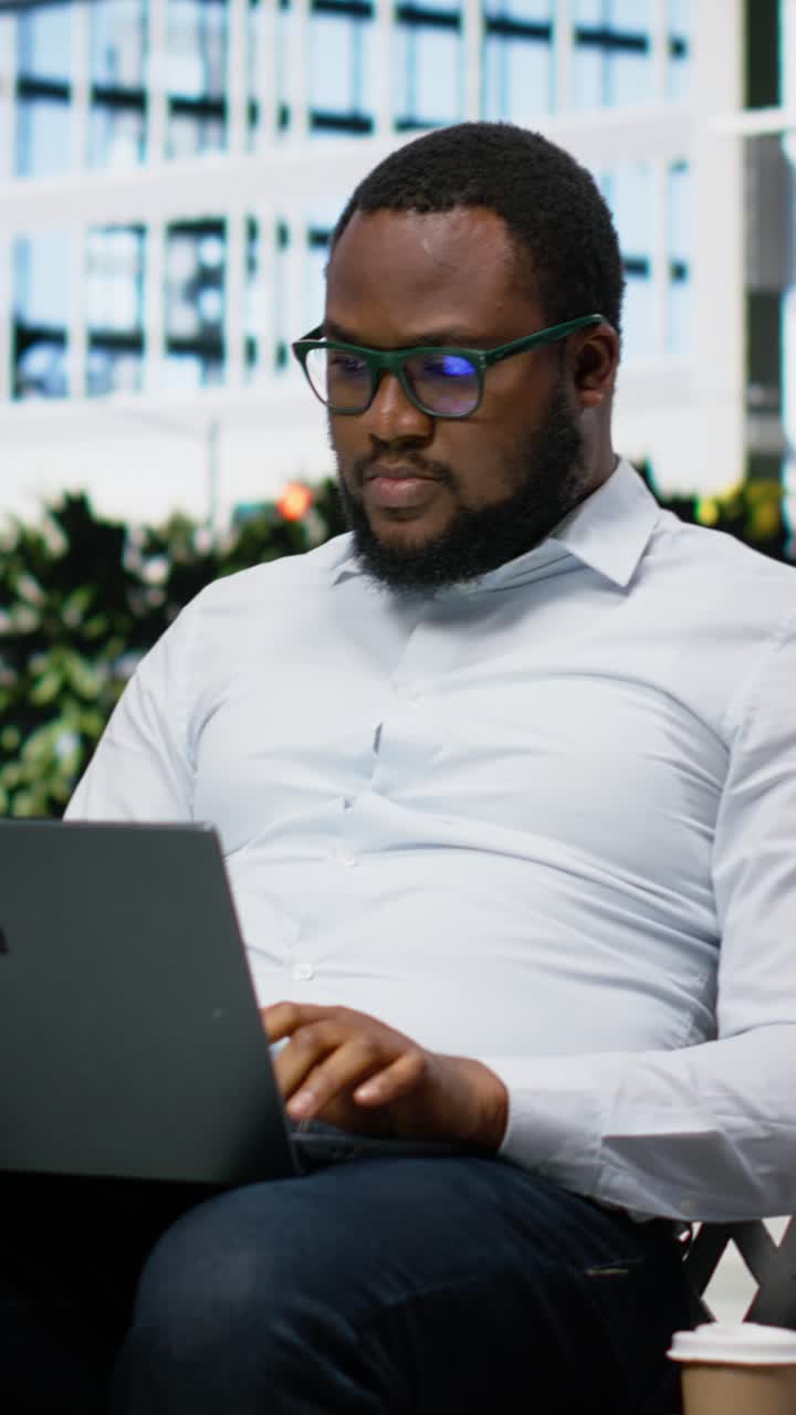 Vertical Video Adult man siting comfortably on a bench navigating a website on his laptop