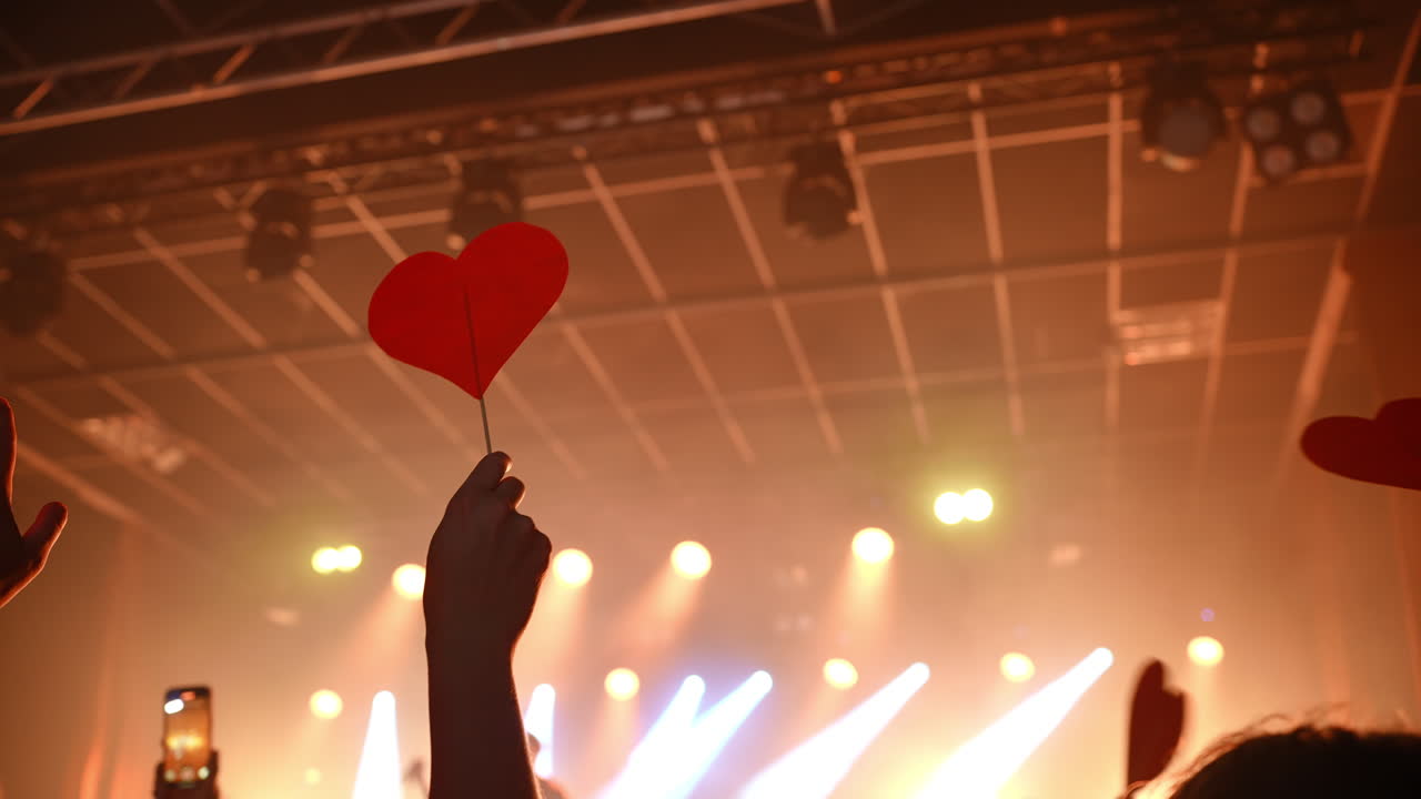 Red paper hearts held by fans create a warm atmosphere of love and appreciation during a live music performance, illuminated by stage lights
