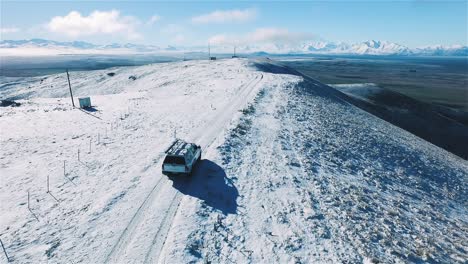 plano general de un coche todoterreno conduciendo por una carretera con montañas blancas como la nieve, monte mackenzie, invierno de la cuenca mackenzie, seguimiento aéreo - tiro de muñeca