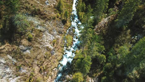 Aerial-flight-above-a-vivid-and-idyllic-mountain-river-waterfall-canyon-with-fresh-blue-water-in-the-Bavarian-Austrian-alps,-flowing-down-a-beautiful-riverbed-along-trees,-forest-and-rocks-from-above