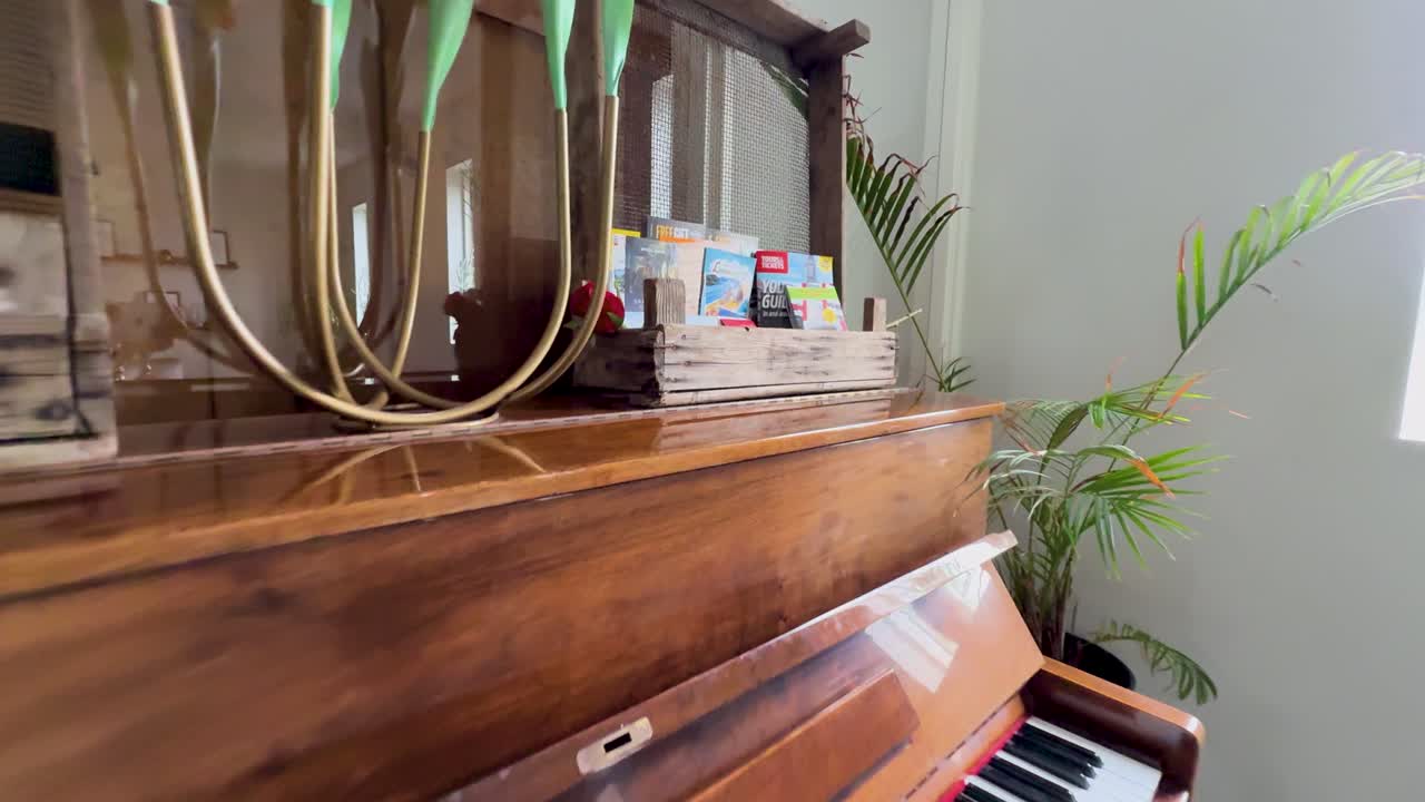 Camera pulls back from a vintage upright piano inside a sunlit contemporary dining area