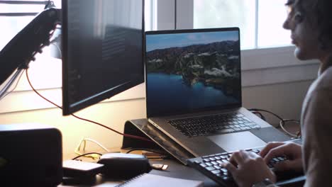 efficient home office: young caucasian man with long curly hair and glasses works on dual screens