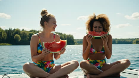 two women enjoying watermelon slices on a lake in summer