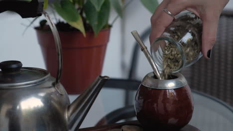 close up slow motion shot of woman hand pouring down yerba into pumpkin mate, preparing the local beverage of argentina and uruguay