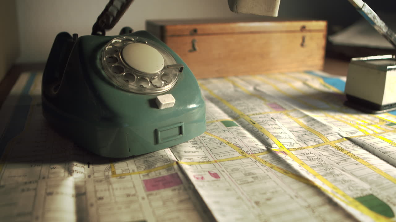 Primo piano di una mano che individua una posizione su una mappa stradale prima di comporre un numero su un telefono vintage. Concetto per il tracciamento di sospetti o il coordinamento della polizia