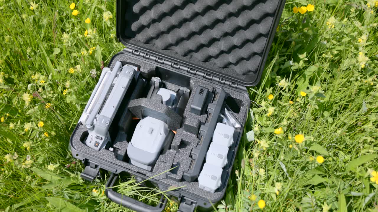Open hard case with drone kit on a green meadow. Camera drone, controller and spare batteries arranged in foam