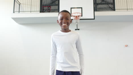 african american boy standing in school gym, looking determined near basketball hoop, copy space