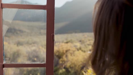 woman opening the window and looking into an amazing scenic landscape with hills, dolly in shot of unrecognizable lady seen from behind