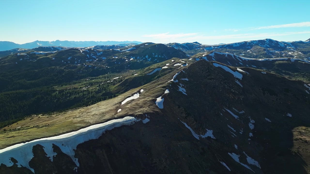 Snoet alpevej, der krydser højfjeldstundra ved Loveland Pass, med en panoramisk drone-tilbagetrækning, der etablerer baggrunden med usikre sneklædte klipper.