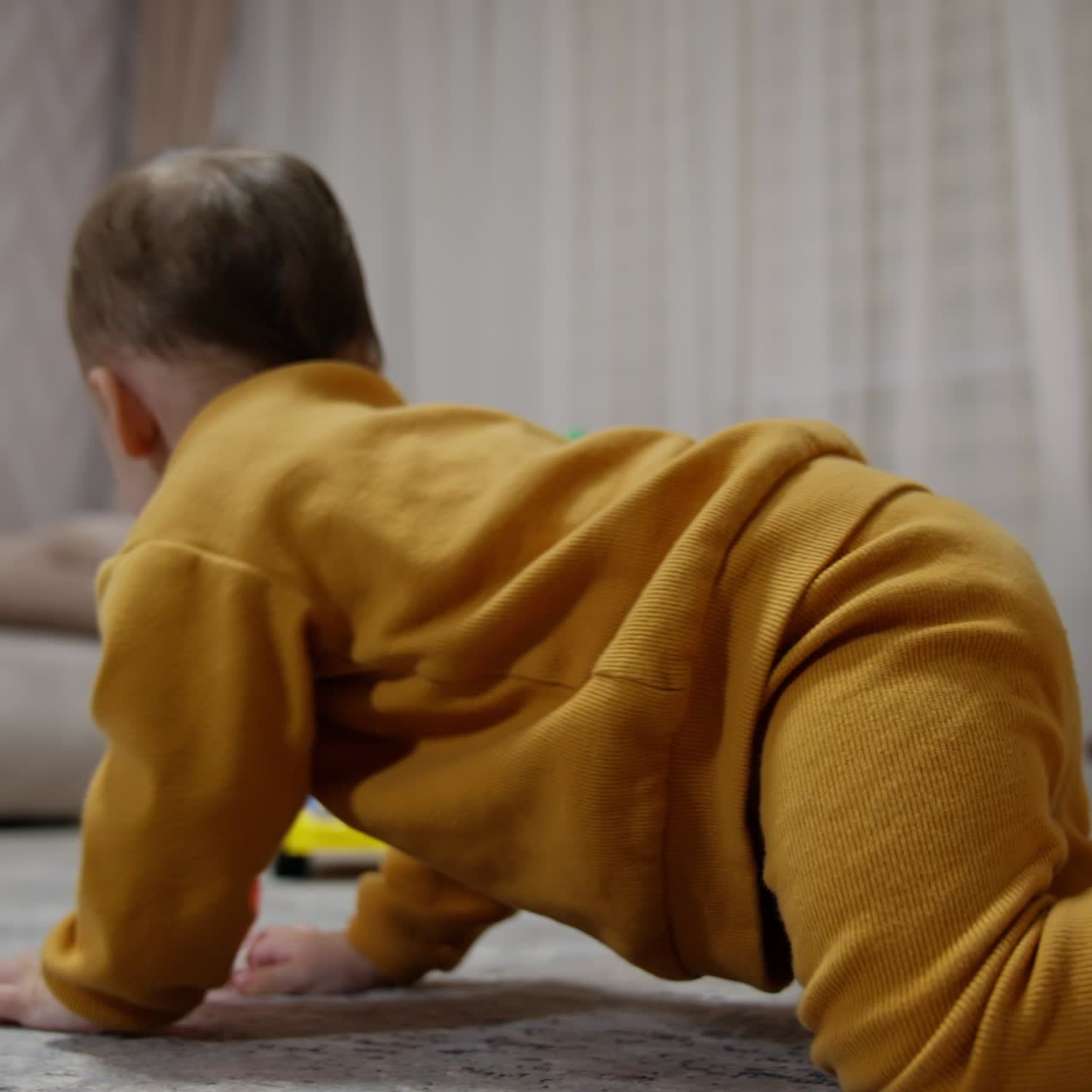 Active Caucasian toddler wearing orange clothes crawls around the room among the toys. Baby follows the red balls kicking it by the floor