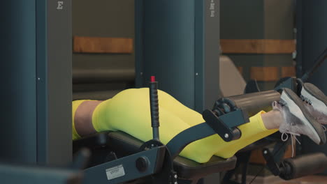 strong hispanic brunette sportswoman doing legs exercise on sport simulator in fitness club. in yellow sportswear. athletic woman performs an extension leg exercise in the simulator