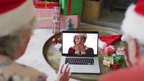 Pareja-Caucásica-Mayor-Con-Sombreros-De-Santa-Usando-Una-Computadora-Portátil-Para-Una-Videollamada-Navideña-Con-Una-Mujer-En-La-Pantalla