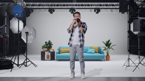 cuerpo lleno de fotógrafo asiático usando una cámara tomando fotos y haciendo un gesto de silencio mientras está de pie en el estudio