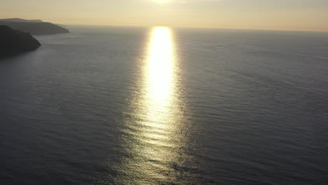 Drone-shot-tilting-down-while-looking-at-the-refection-of-sun-rays-on-the-ocean-from-sunset-on-the-North-Devon-coast-in-the-UK