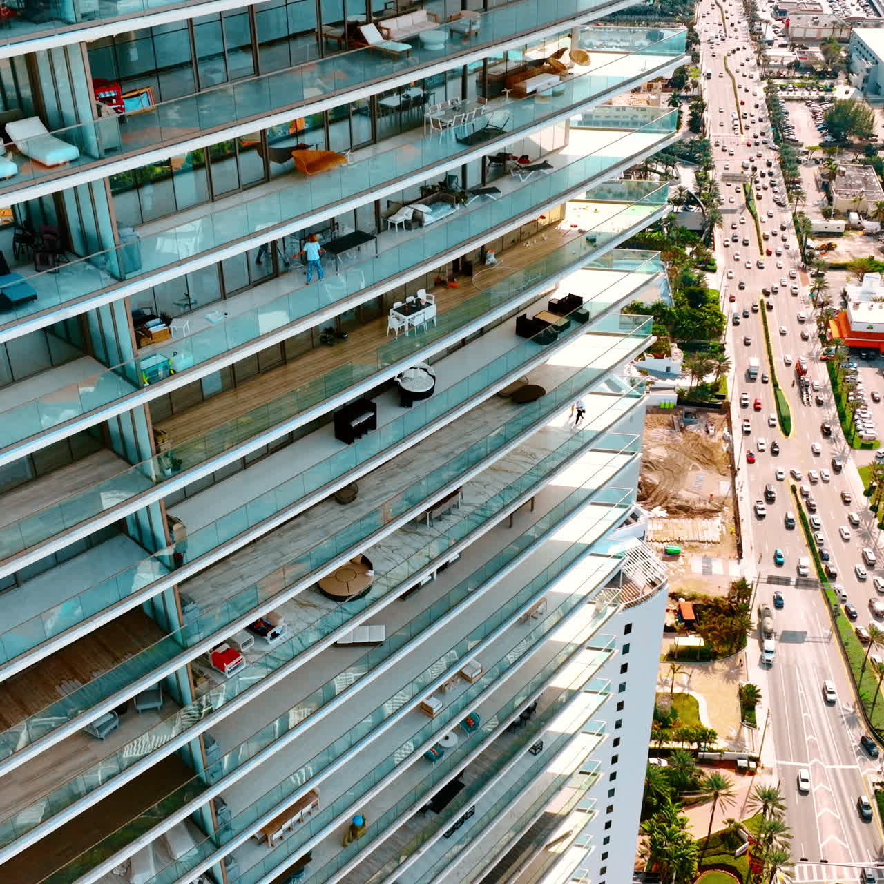 Rising along the multi-storied apartment block with large open balconies. Street with busy highway at the foot of the building. Top view on Miami Beach, Florida, USA.