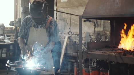 herrero en casco, hierro de soldadura en el taller