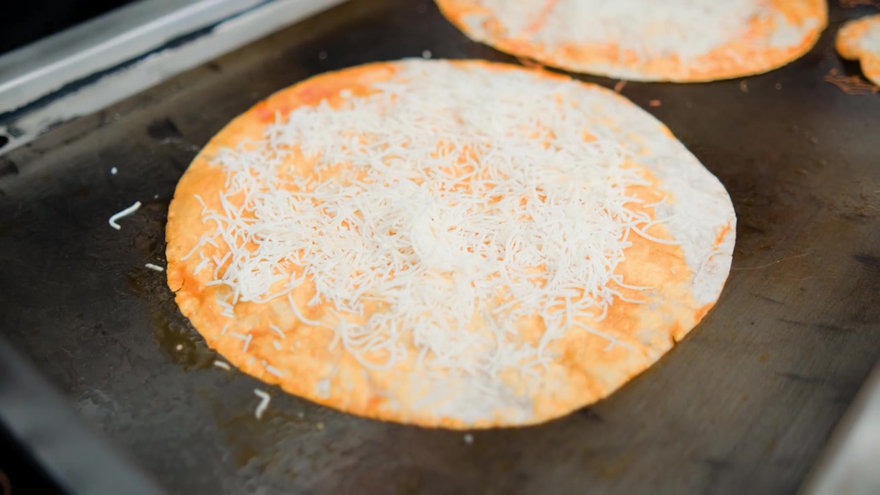 Commercial kitchen footage showing birria pizza tortillas preparation for birria pizza during preparation of a savory birria pizza on a flat grill