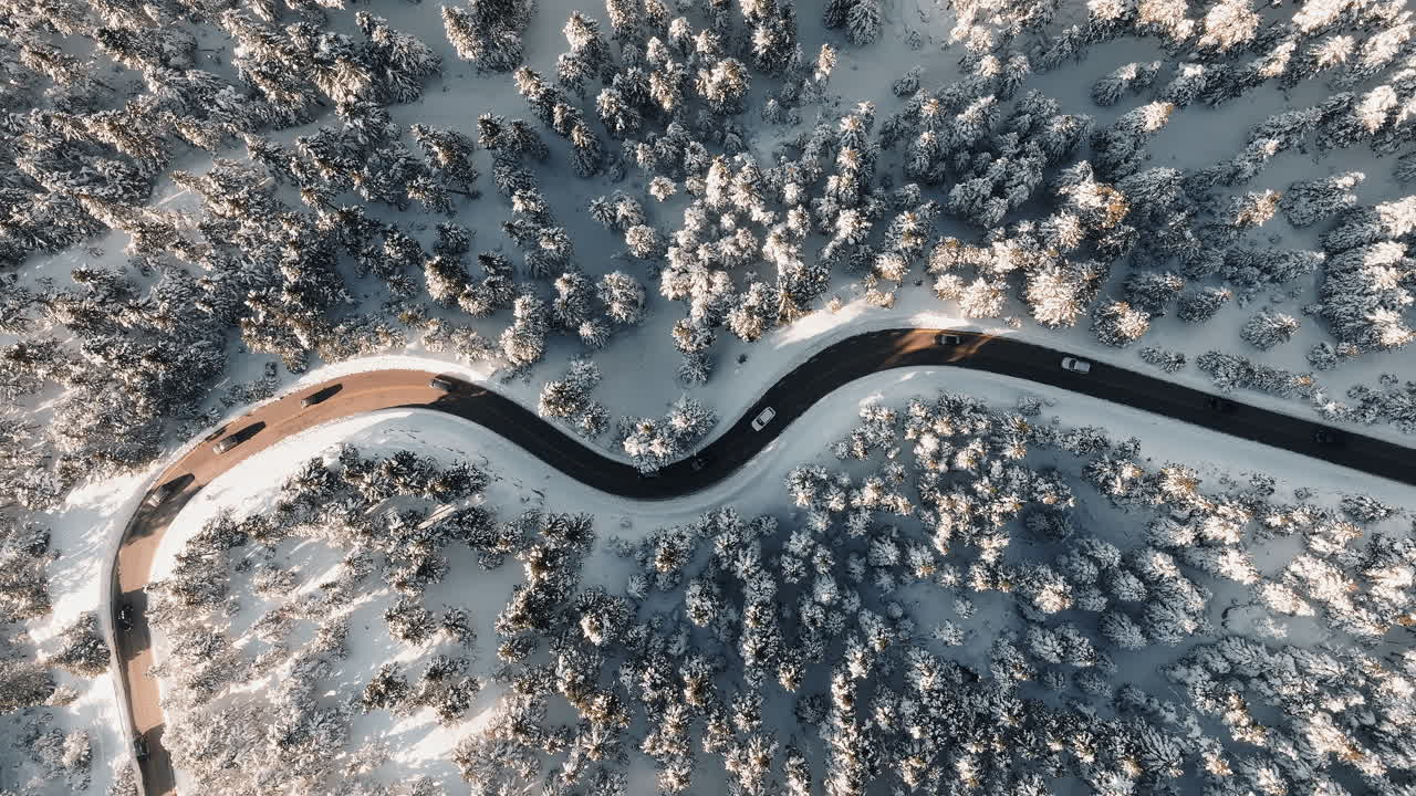 Top down drone shot of a winding mountain road on Mount Parnassus during winter, surrounded by snow-covered fir trees on a sunny day