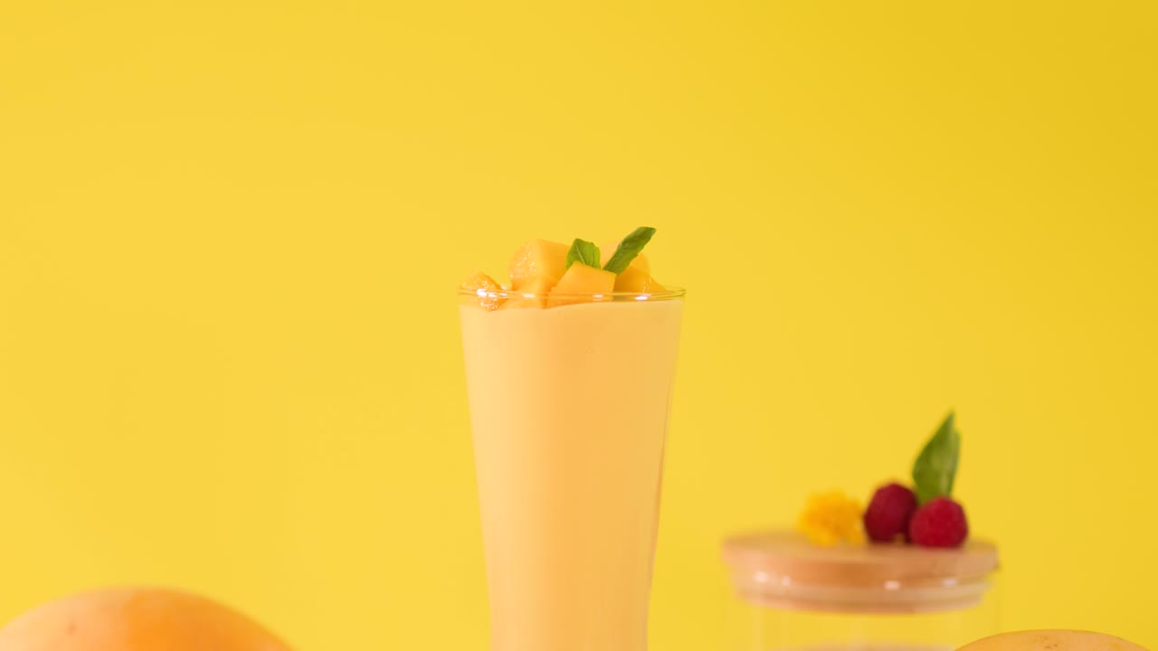 Una mano umana decora un frullato di mango alto con una guarnizione di frutta divertente su uno sfondo giallo brillante