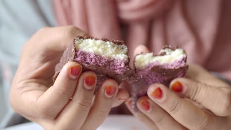 close-up of a woman's hands holding a broken chocolate bar with coconut and purple filling