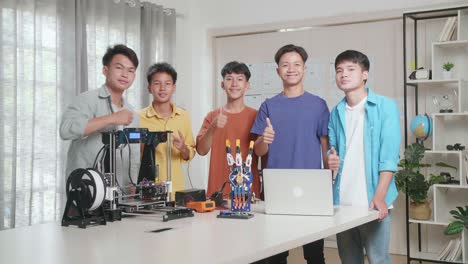 group of young asian boys with a laptop and 3d printing smiling and showing thumbs up gesture to the camera while discussing about a cyborg hand at home