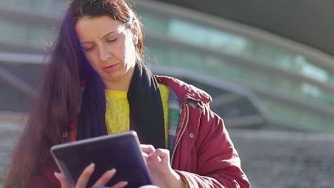 Focused-middle-aged-woman-with-long-dark-hair-using-tablet