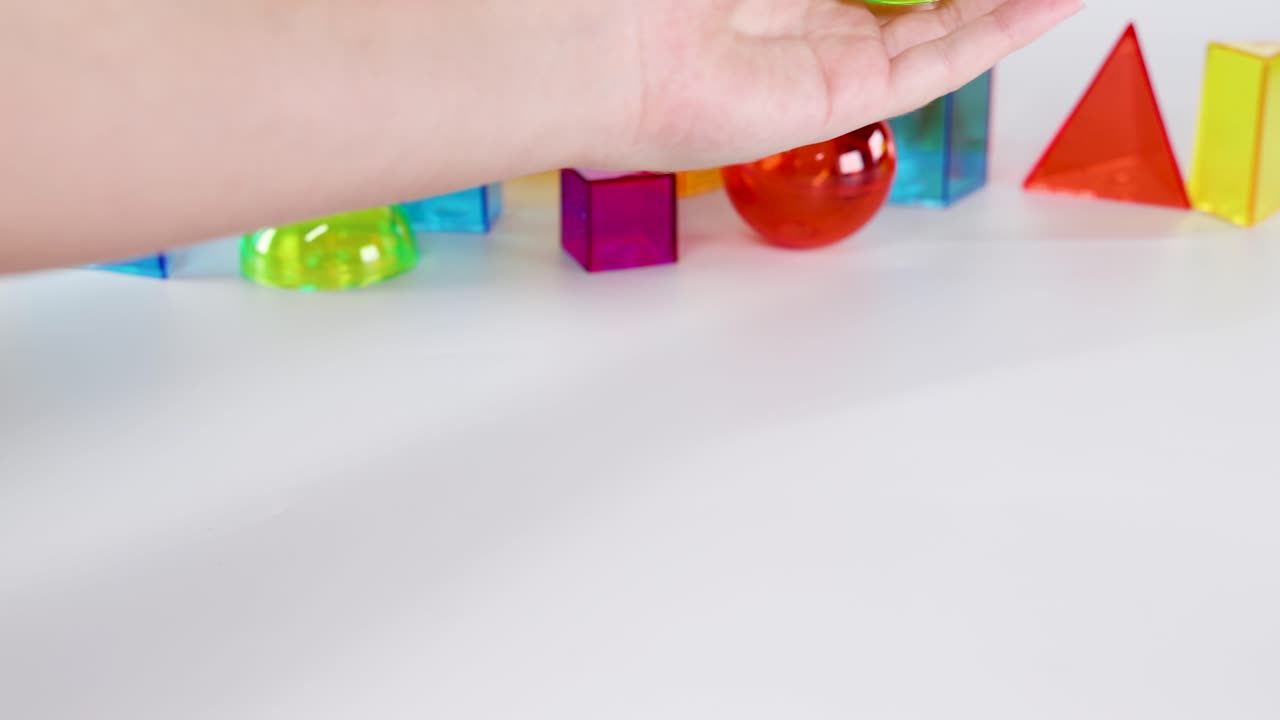 A hand interacts with vibrant 3D geometric shapes on a white background, demonstrating movement and balance