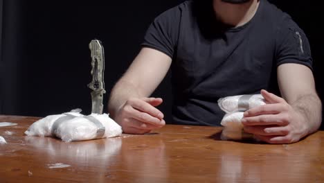 cropped image of a drug dealer sitting by the table with packs of cocaine for trading with money