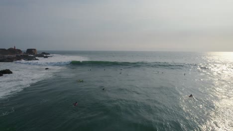 Surfers-surfing-next-to-rocks,-over-rough-sea-with-waves,-Aerial-shot-forward-to-horizon