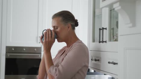 mujer caucásica mayor con camisa rosa y una taza de café en la cocina