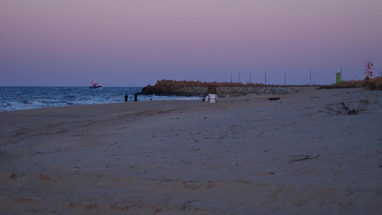 Folk spadserer på Władysławowo strand i skumringen. Fiskerbåd i baggrunden, der vender tilbage til havnen. Polen.