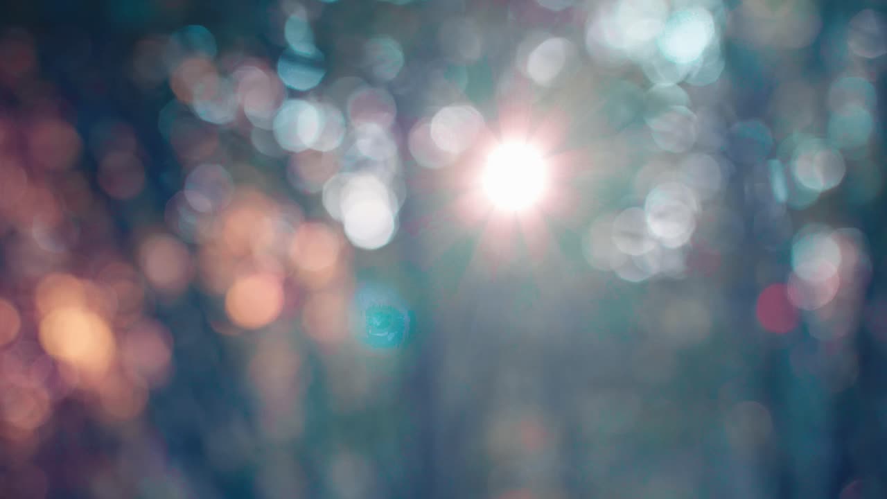Luci bokeh sfocate di una foresta creano uno sfondo astratto naturale. La luce solare sfocata filtra attraverso gli alberi, producendo sfere luminose e tenui di colori bianco, verde acqua e arancione per transizioni da sogno