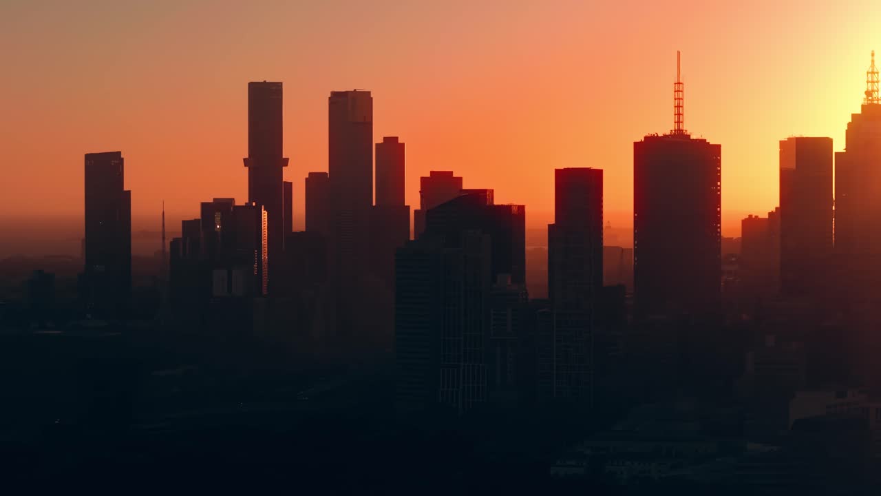 Atardecer aéreo sobre el horizonte de Melbourne desde Abbotsford con la ciudad silueteada en un resplandor naranja, estableciendo un metropolitano australiano urbano y abstracto, paneando a la derecha