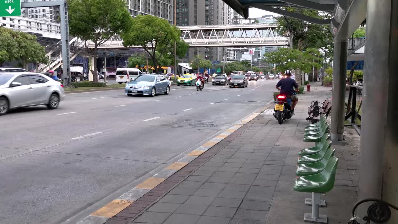 4K Illegal Motorcyclist Driving Wrong Way on Sidewalk Next to Bus Stop with Vehicle Traffic Along Ratchadaphisek Road in Bangkok, Thailand.