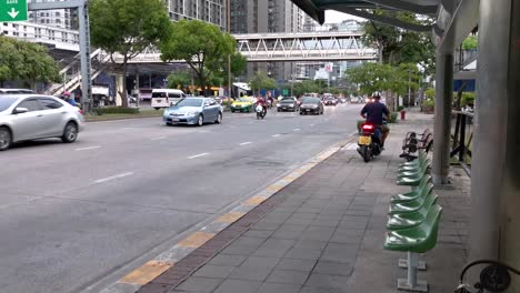 4k illegal motorcyclist driving wrong way on sidewalk next to bus stop with vehicle traffic along ratchadaphisek road in bangkok, thailand.