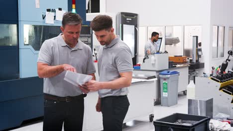 ingeniero y aprendiz discuten planes en el piso del taller de ingeniería