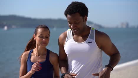 multiethnic couple in sportswear jogging along embankment