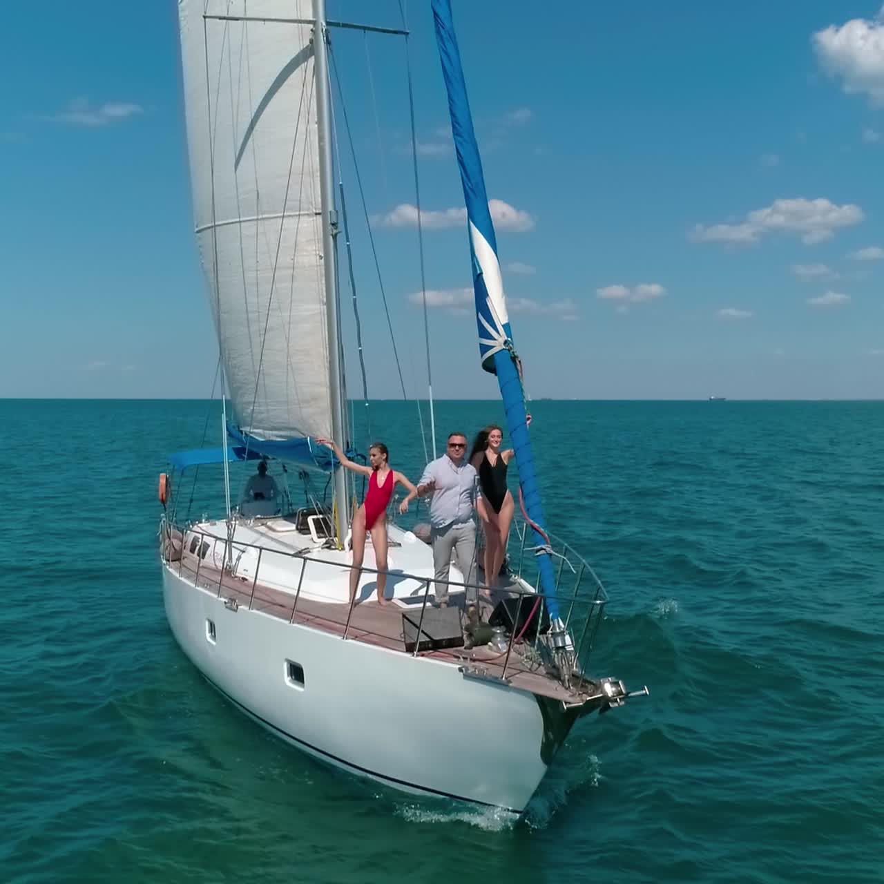 Sea voyage on a yacht. Man and young women sing and dance on a sail boat in the open sea. People spend joyful time on a small ship in summer