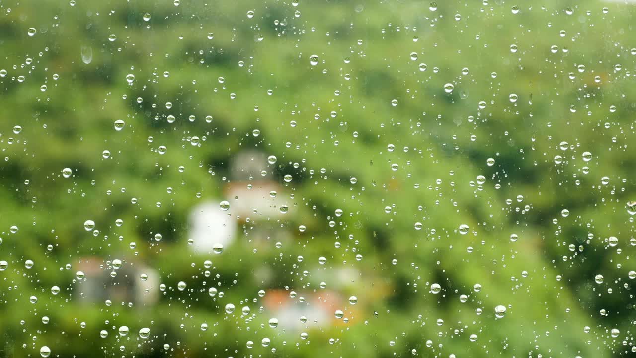 raindrops on glass window at the backdrop of green mountains