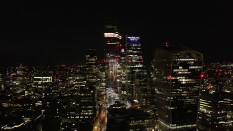 Backwards-fly-above-urban-district.-Elevated-view-of-group-of-modern-skyscrapers-at-night.-London,-UK