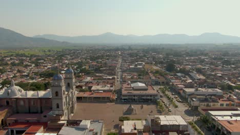 wide aerial view of tuxpan jalisco with church, plaza, city market and distant mountains. slow dolly in droneshot