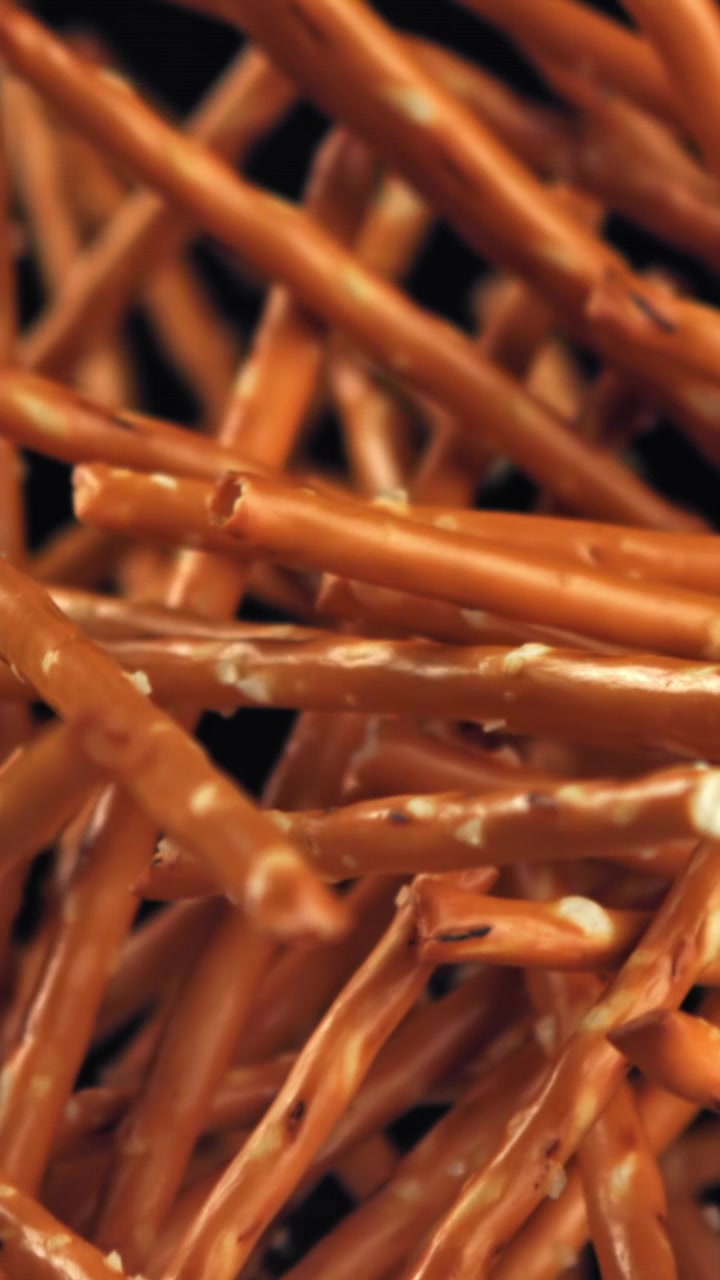 Bastoncini di pretzel salati che cadono al rallentatore su sfondo nero.